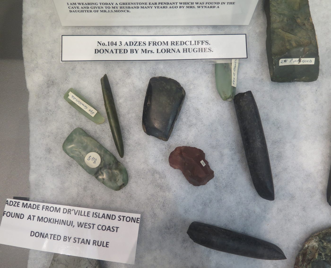 Adzes and stone tools laid out with donor labels, including pounamu pieces